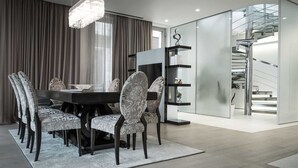 A modern dining room with a round table, patterned chairs, a chandelier, and a staircase with glass railings. - Dukley Penthouse 3 Bedrooms (Budva)