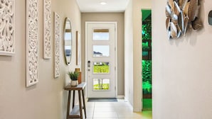 A hallway with a door, framed artwork, a small table with a plant, and a green-lit wall. - Lux Jungle Bunks/Pool/Solara Resort/Sleep 14 (Kissimmee)