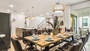 A modern dining area with a long wooden table, leather chairs, and pendant lighting. - Lux Jungle Bunks/Pool/Solara Resort/Sleep 14 (Kissimmee)