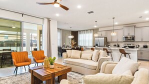 A modern living room with a sofa, coffee table, and chairs, a kitchen with appliances, and a dining area. - Lux Jungle Bunks/Pool/Solara Resort/Sleep 14 (Kissimmee)