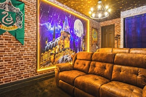 Una habitación con pared de ladrillo, un gran mural iluminado con temática de Hogwarts, un sofá de cuero y una araña.