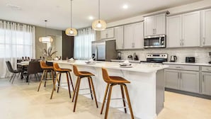 A modern kitchen with a central island, bar stools, stainless steel appliances, and light-colored cabinetry. - Lux Jungle Bunks/Pool/Solara Resort/Sleep 14 (Kissimmee)