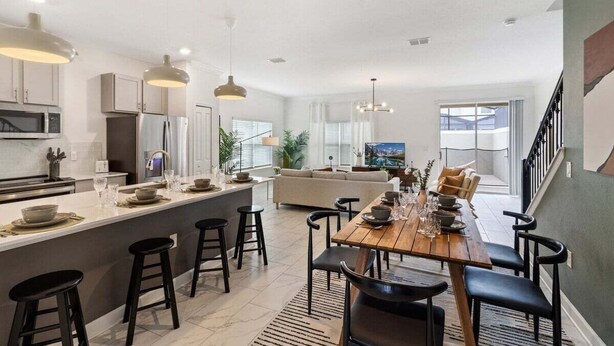 A modern kitchen with a central island, bar stools, and a dining area with a wooden table and chairs. - 20% OFF Weekly Stay/ 5BR/Free Water Park (Kissimmee)