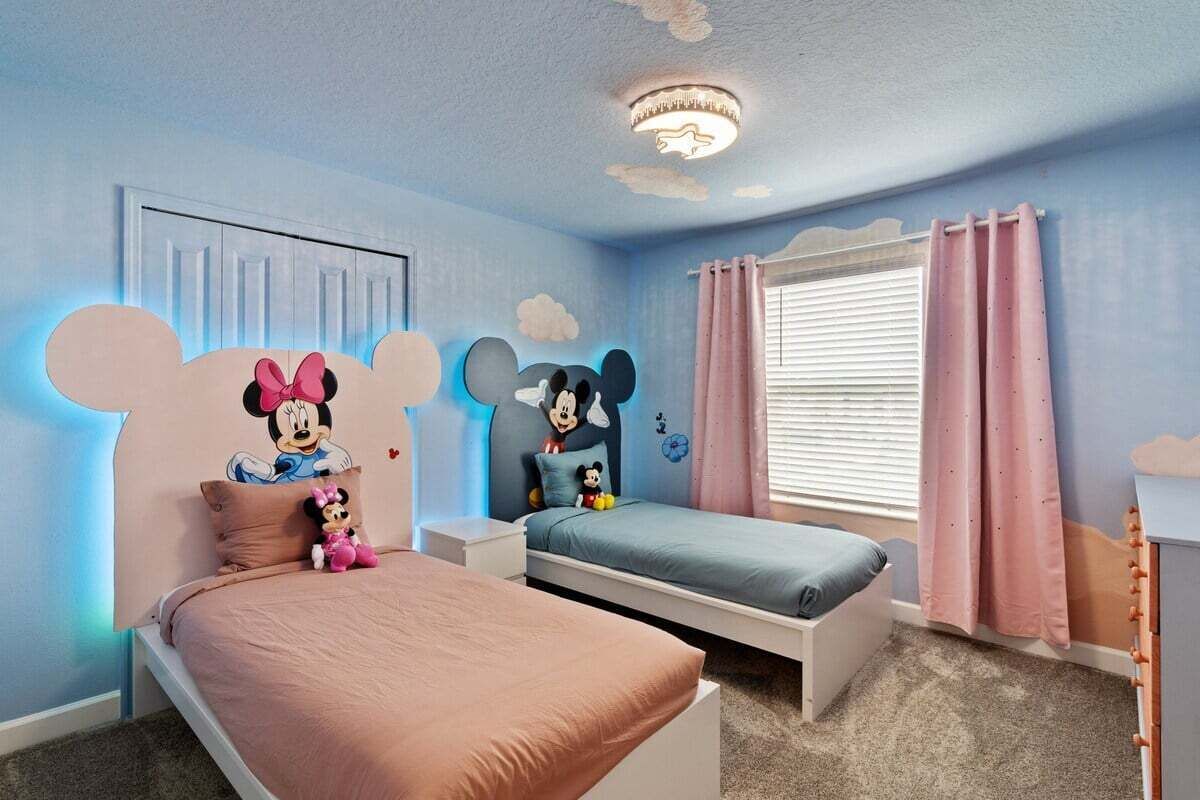A children's room with two beds, one with a Mickey Mouse headboard and another with a Minnie Mouse headboard, both featuring plush toys.