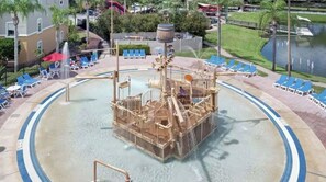Parque acuático con una estructura central de juegos, zona de piscina circundante y sillas de descanso.