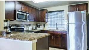 Una cocina con armarios de madera oscura, electrodomésticos de acero inoxidable, encimeras de granito y una ventana con persianas.