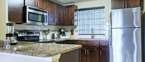 A kitchen with dark wooden cabinets, stainless steel appliances, granite countertops, and a window with blinds.