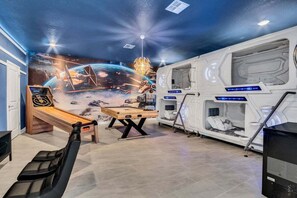 Une pièce décorée d’une fresque murale sur le thème de Star Wars, avec une table de jeux, un fauteuil inclinable et un lit futuriste.