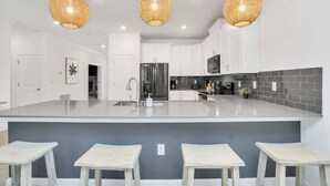 Una cucina moderna con isola centrale, mobili bianchi, frigorifero in acciaio inossidabile e tre lampade a sospensione in vimini.