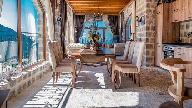 Un'accogliente stanza con soffitto in legno, pareti in pietra, angolo ristoro con tavolo e sedie, e angolo cottura.