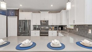 A modern kitchen with white cabinets, stainless steel appliances, and a central island with blue placemats. - Brand New Storey Lake 8BR Villa with Lake View (Kissimmee)