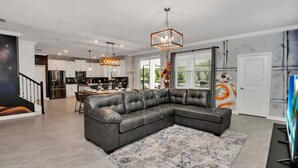 A modern living room with a sectional sofa, a dining area, and a kitchen in the background. - Brand New Storey Lake 8BR Villa with Lake View (Kissimmee)