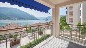 Un balcon offrant une vue sur un lac et des montagnes, agrémenté d’une auvent bleue et de rampes en métal.