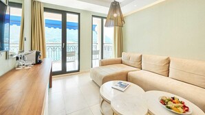 Un moderno salón con un sofá color beige, una mesa de centro redonda y una mesa de comedor con un frutero. Hay grandes puertas correderas de vidrio que dan a un balcón con vistas al mar.