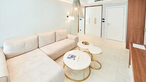 Una sala de estar moderna con un sofá color beige, dos mesas redondas con patas doradas y un espejo grande que refleja un armario y una puerta.