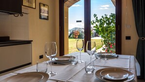 Tavola imbandita per quattro, con piatti, posate e bicchieri da vino, affacciata su un giardino con una serra.