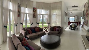Ein geräumiges Wohnzimmer mit einer großen Sofagarnitur, einem runden Hocker und einem Essbereich mit Tisch und Stühlen.