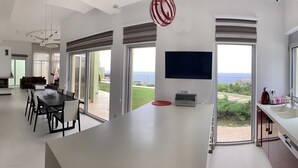Eine moderne Küche mit einer großen Kochinsel, einem Flachbildfernseher und großen Fenstern mit Blick auf das Meer.