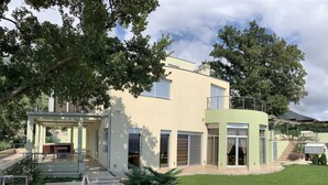 Ein modernes, zweistöckiges Haus mit einer überdachten Terrasse, einem kleinen Garten und einer Treppe zum Eingang.