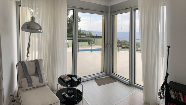 Ein modernes Zimmer mit einer großen Schiebetür zum Poolbereich, einer gemütlichen Sitzecke mit Sofa und kleinem Tisch sowie einer Lampe.