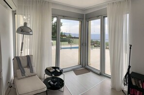 A modern room with a large sliding glass door leading to a pool area, a comfortable seating area with a sofa and a small table, and a lamp. - Hidden jewel Villa Gem (Bar)