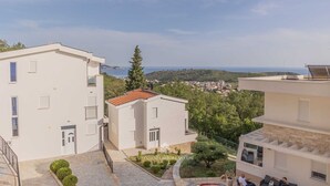 Un immeuble résidentiel doté d’une cour pavée de pierres, offrant une vue sur la mer et s’ouvrant sur un ciel dégagé.
