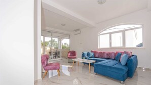 Un salon spacieux avec un canapé bleu, un fauteuil rose et une table basse blanche.