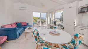 Un salon moderne avec un canapé bleu, une table à manger ronde et un coin cuisine équipé d’un four à micro-ondes.