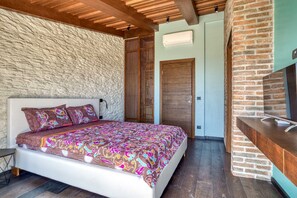 Ein Schlafzimmer mit einem gemusterten Bettbezug, einer Holzbalkendecke, einer Steinwand und einer Backsteinwand.