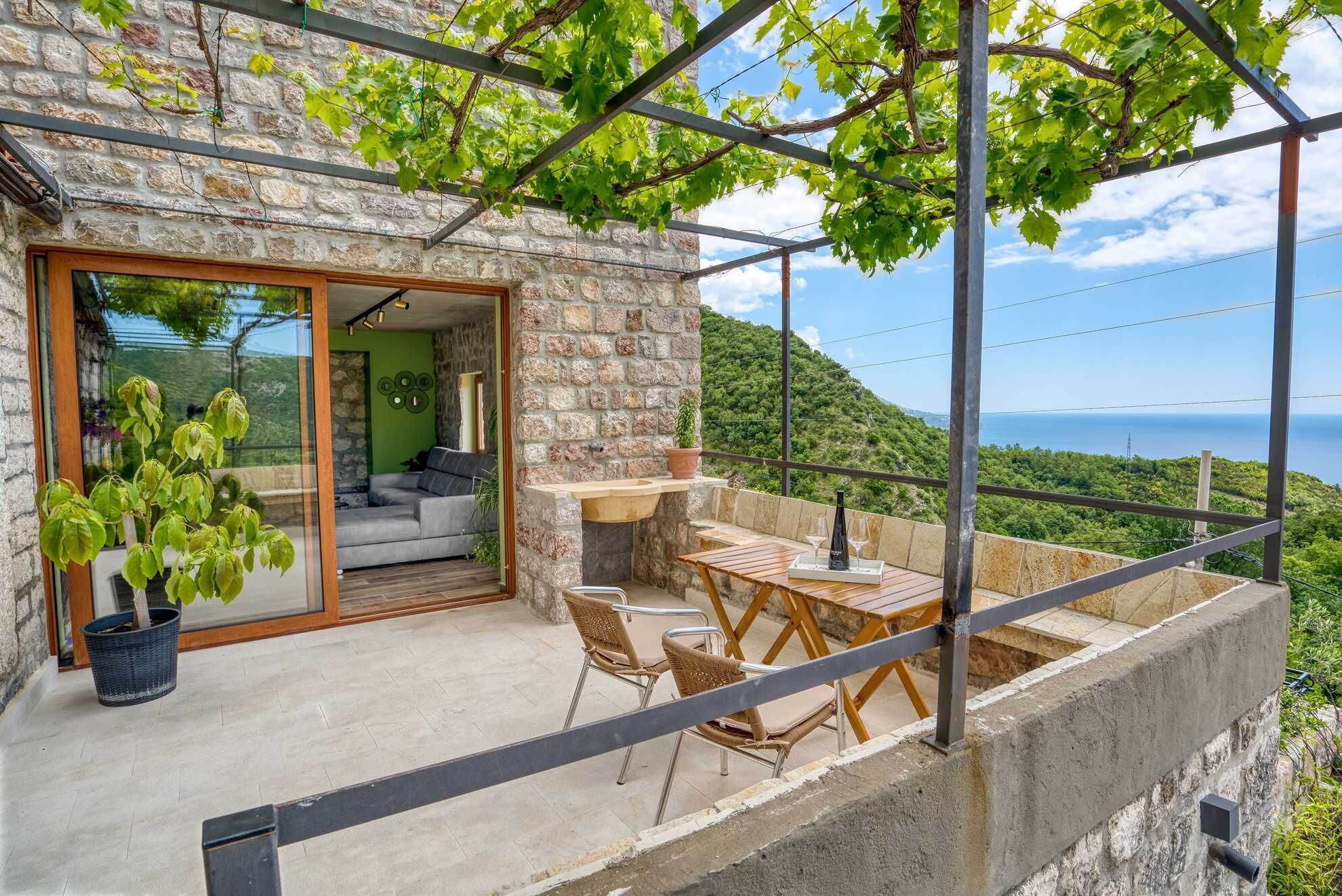 Une maison en pierre dotée d’un balcon, d’un coin repas avec une table et des chaises, et offrant une vue sur la mer.