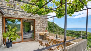 A stone house with a balcony, a dining area with a table and chairs, and a view of the sea. - Green Haven 2 Bedrooms (Budva)