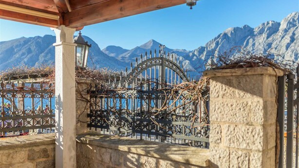 Un muro di pietra con un cancello in metallo e un pergolato in legno.