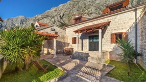 Un edificio in pietra con tetto a tegole, un piccolo giardino e montagne sullo sfondo.