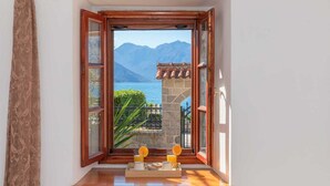 Una stanza con davanzale in legno, un piccolo tavolo con cose per la colazione e vista sulle montagne e un lago.