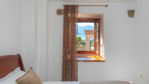 Una camera da letto con un letto, una finestra che si affaccia su un edificio e montagne, e una tenda.