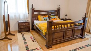 Quarto com cama de madeira, mesa de cabeceira, cômoda e espelho.