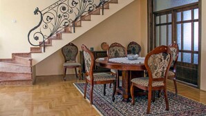 Uma sala de jantar com uma mesa e cadeiras de madeira, um tapete estampado e uma escada com grades de metal decoradas.
