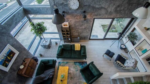 Un espacio habitable moderno estilo loft, con un ventanal grande, un sofá verde, una mesa de centro y una estantería.