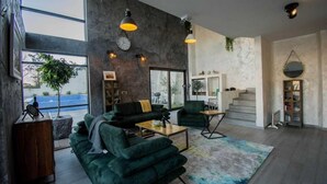 Una sala de estar moderna con un ventanal grande, un sofá verde, una mesa de centro y una escalera que conduce a un nivel superior.