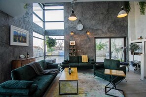 Un salon spacieux avec une grande fenêtre, un canapé vert, une table basse et une bibliothèque.