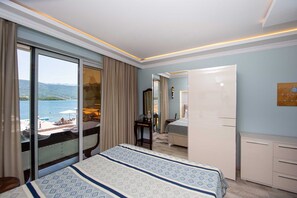 Une chambre d’hôtel avec un grand lit, un bureau, une chaise, une armoire et une vue sur la plage et la mer.