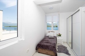 Ein Schlafzimmer mit Bett, Nachttisch, Kommode und Blick auf einen See und Berge.