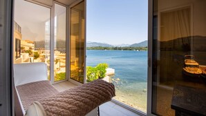 Una camera da letto con un'ampia porta scorrevole in vetro che si apre su un balcone con vista su un lago e montagne sullo sfondo.