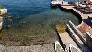 Un lago limpido con barche ormeggiate, un molo con lettini prendisole e montagne sullo sfondo.
