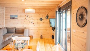 Un interior de madera acogedor con un sofá, una mesa de comedor para dos personas y un ventanal con un ventilador.