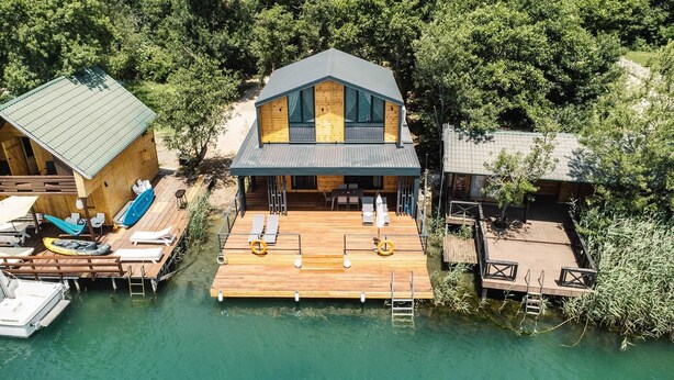 Una casa de madera con un muelle, asientos al aire libre y un bote.