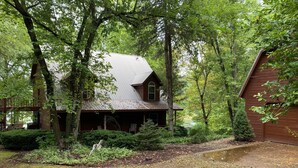 A rustic cabin with a metal roof, surrounded by dense forest. - Beaver Lake Paradise with Bunkhouse (Springdale)