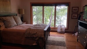 A bedroom with a large bed, a window with a view of trees, a fan, and a dresser. - Beaver Lake Paradise with Bunkhouse (Springdale)