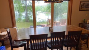 A dining area with a large wooden table and four chairs, a window with a view of a garden, and a chandelier. - Beaver Lake Paradise with Bunkhouse (Springdale)