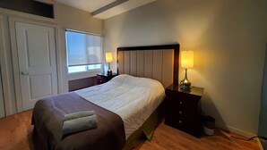 Un dormitorio ordenado con una cama grande, dos mesitas de noche con lámparas, una ventana y una puerta.